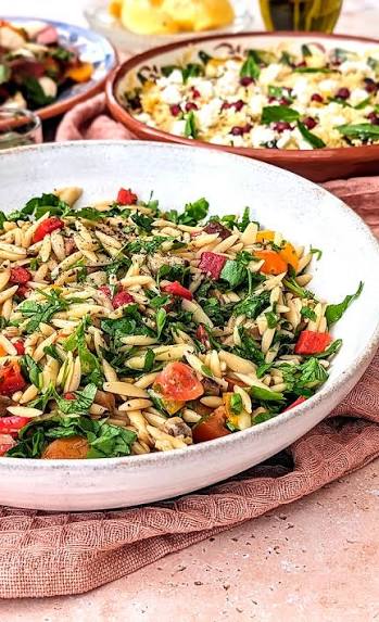 Orzo salade met kruiden en tomaten naast een schaal met feta en granaatappel